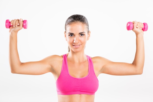 Retrato de uma jovem mulher bonita se exercitando com halteres. Ela está praticando o grupo muscular da parte superior do corpo.