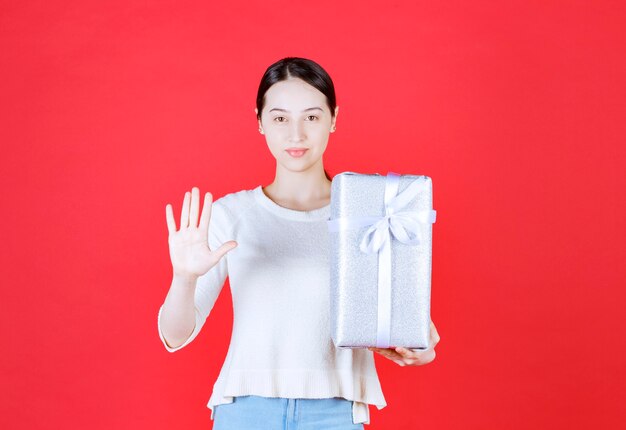 Retrato de uma jovem mulher bonita segurando uma caixa de presente e gesticulando para parar