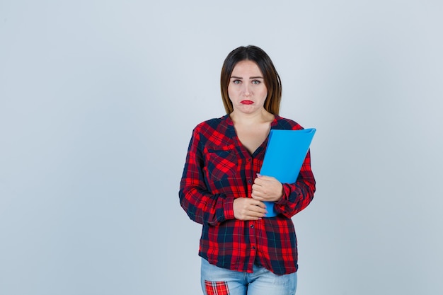 Retrato de uma jovem mulher bonita segurando uma pasta com uma camisa casual e olhando desapontada com a vista frontal