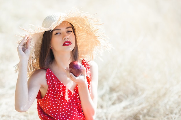 Foto retrato de uma jovem mulher bonita usando chapéu de palha no verão. fêmea com maçãs frescas na natureza.