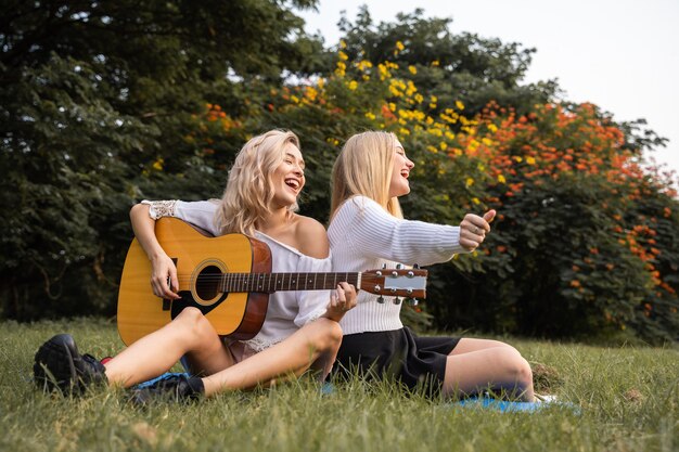 Retrato de uma jovem mulher branca sentada no parque ao ar livre, tocando um violão e cantando uma música junto com a felicidade