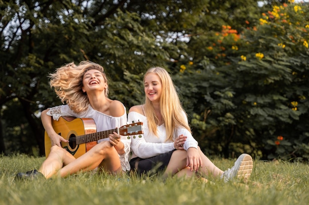 Retrato de uma jovem mulher branca sentada no parque ao ar livre, tocando um violão e cantando uma música junto com a felicidade