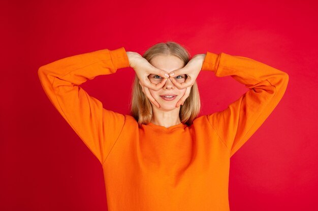 Retrato de uma jovem mulher caucasiana com emoções brilhantes, isolada no fundo vermelho do estúdio