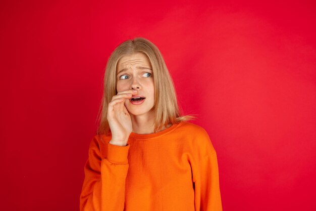 Retrato de uma jovem mulher caucasiana com emoções brilhantes, isolada no fundo vermelho do estúdio