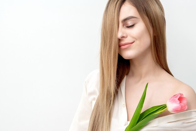 Retrato de uma jovem mulher caucasiana feliz com os olhos fechados e uma tulipa rosa contra um fundo branco com espaço de cópia