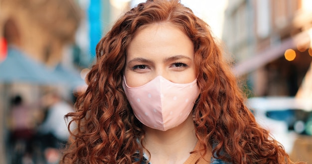 Retrato de uma jovem mulher caucasiana, usando máscara médica protetora no rosto, olhando para a câmera.