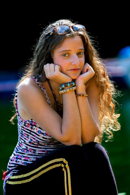 Foto retrato de uma jovem mulher com as mãos no queixo sentada ao ar livre