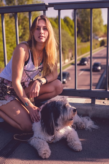 Retrato de uma jovem mulher com um cachorro sentado junto a uma grade na ponte pedonal