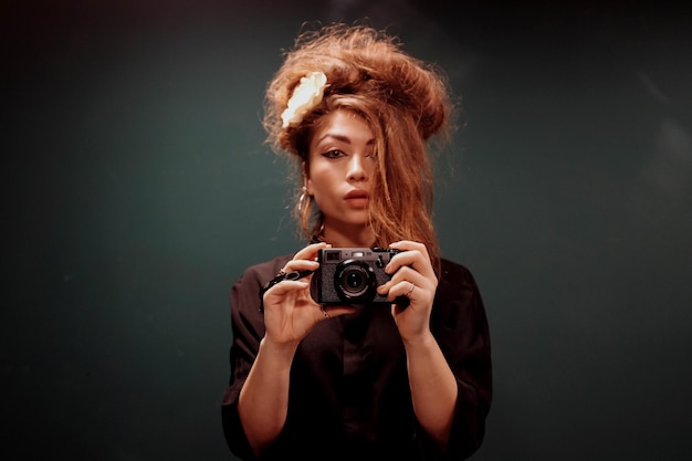 Retrato de uma jovem mulher com uma câmera contra um fundo preto
