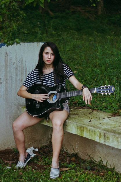 Foto retrato de uma jovem mulher com uma guitarra sentada ao ar livre