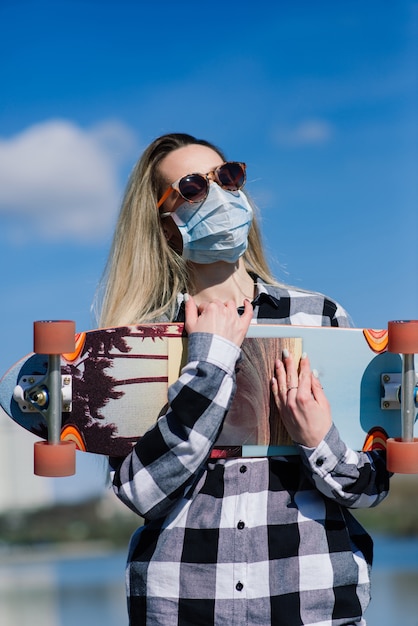 Retrato de uma jovem mulher com uma máscara médica com longboard na cidade