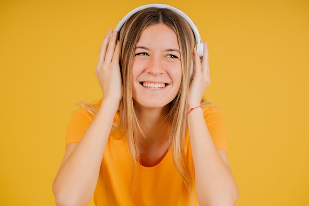 Retrato de uma jovem mulher curtindo ouvir música com fones de ouvido em pé contra um fundo amarelo isolado.