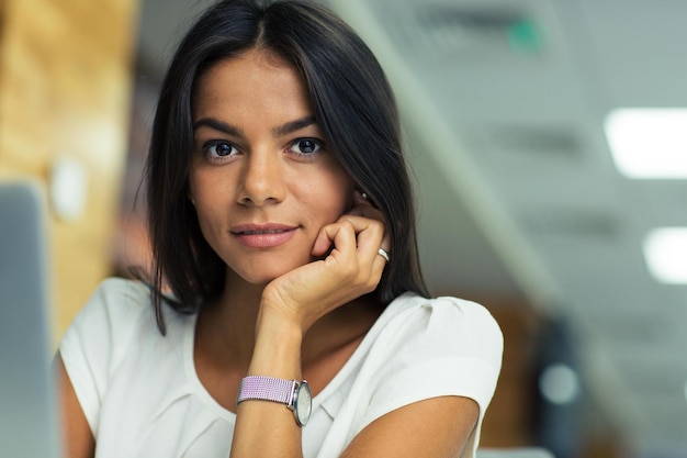 Retrato de uma jovem mulher de negócios bonita no escritório, olhando para a câmera