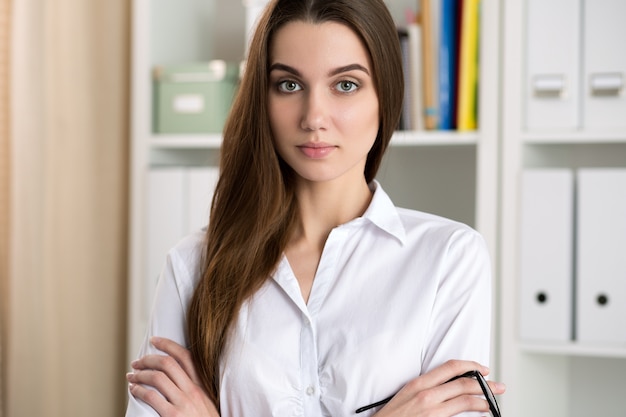 Retrato de uma jovem mulher de negócios em seu escritório com os braços cruzados