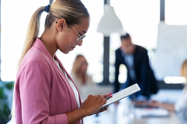 Retrato de uma jovem mulher de negócios inteligente trabalhando com tablet digital no lugar de coworking.