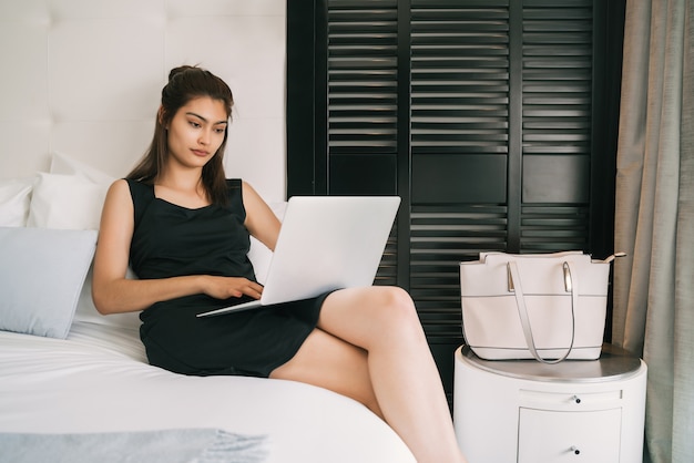 Retrato de uma jovem mulher de negócios trabalhando em seu laptop no quarto do hotel.