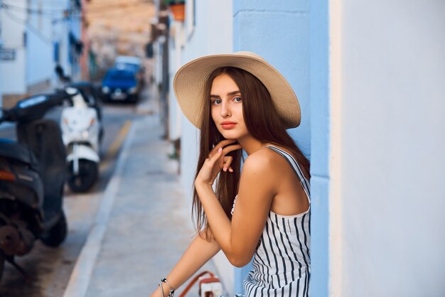 Retrato de uma jovem mulher elegante com chapéu de palha, sentado na rua.