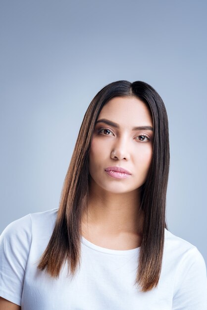 retrato de uma jovem mulher em uma camiseta branca posando contra uma parede cinza