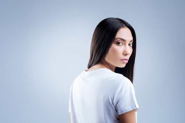 retrato de uma jovem mulher em uma camiseta branca posando contra uma parede cinza