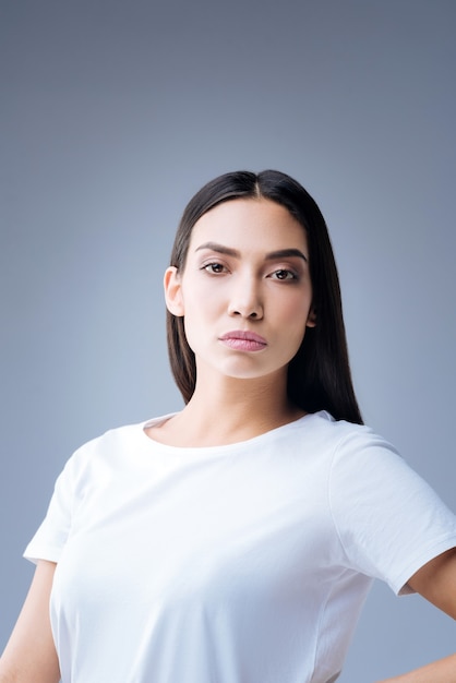 retrato de uma jovem mulher em uma camiseta branca posando contra uma parede cinza