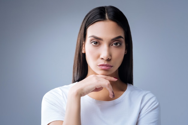 retrato de uma jovem mulher em uma camiseta branca posando contra uma parede cinza