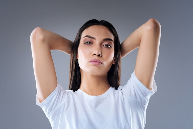 retrato de uma jovem mulher em uma camiseta branca posando contra uma parede cinza