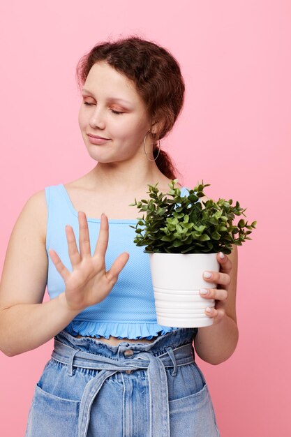 Retrato de uma jovem mulher em vaso de flores posando planta fundo rosa inalterado