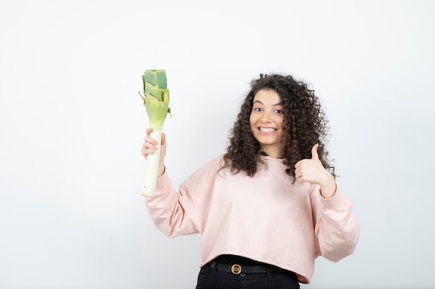 Retrato de uma jovem mulher encaracolada de suéter rosa com aipo desistindo de polegares.