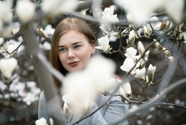 Retrato de uma jovem mulher entre as árvores de magnólia em flor no jardim botânico de Kiev. Árvores de magnólia em flor atraem milhares de visitantes a cada primavera