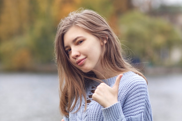 Retrato de uma jovem mulher feliz e positiva, uma adolescente mostrando o polegar, tipo, gesto de aprovação e sorrindo no parque outono