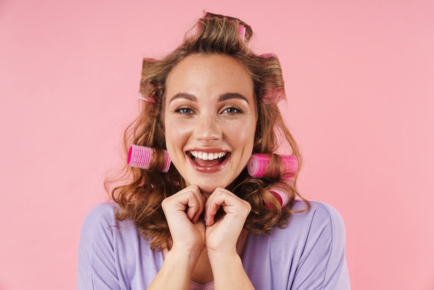 Retrato de uma jovem mulher feliz em bobes sorrindo isolado na rosa