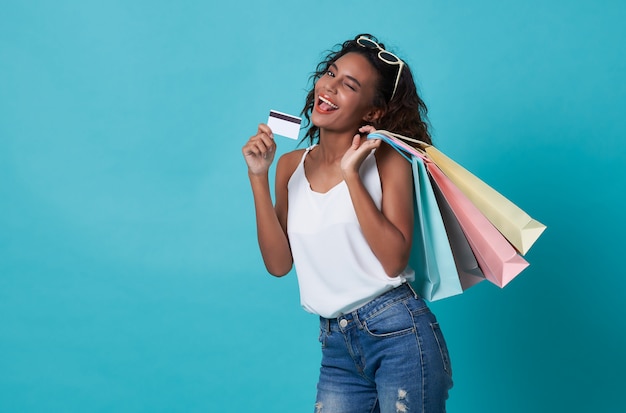 Retrato de uma jovem mulher feliz que mostra o cartão e o saco de compras de crédito isolados sobre o fundo azul.