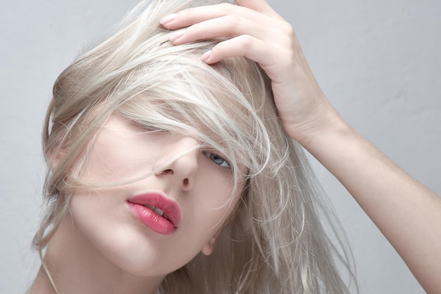 Retrato de uma jovem mulher loira bonita com lábios vermelhos gordos toca seu cabelo em um close-up de fundo branco. Penteado elegante na moda