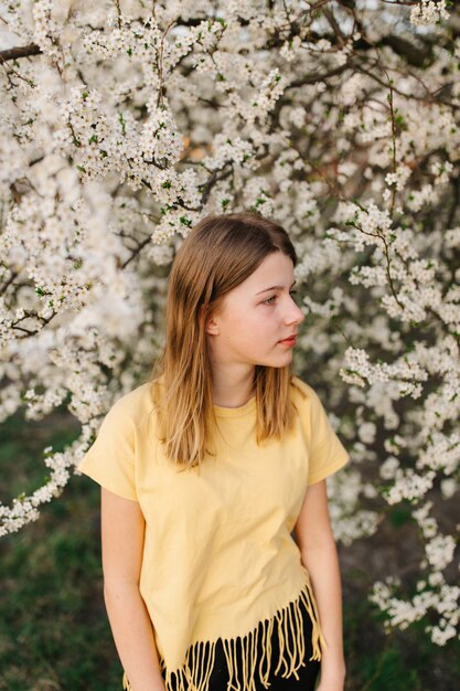 Retrato de uma jovem mulher loira bonita perto de árvore florescendo com flores brancas em um dia ensolarado.