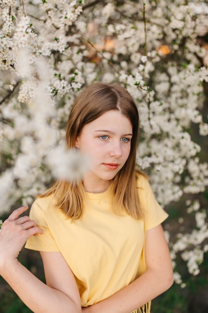 Retrato de uma jovem mulher loira bonita perto de árvore florescendo com flores brancas em um dia ensolarado.