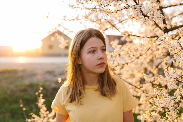 Retrato de uma jovem mulher loira bonita perto de árvore florescendo com flores brancas em um dia ensolarado