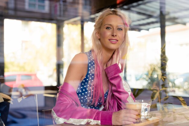 Retrato de uma jovem mulher loira bonita relaxando na cafeteria pela janela de vidro