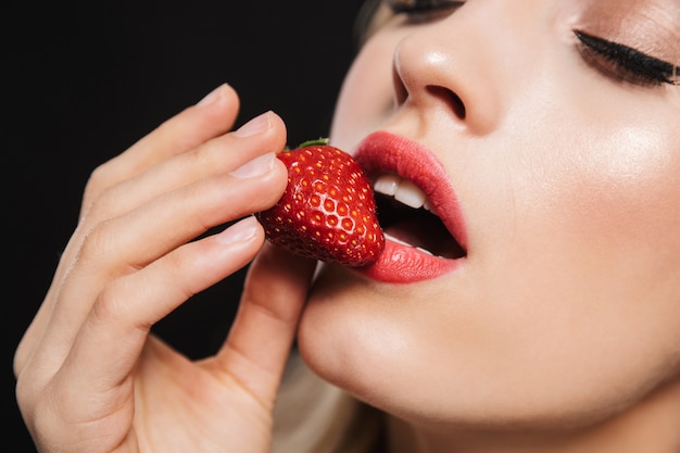 Foto retrato de uma jovem mulher loira com lábios vermelhos de maquiagem brilhante posando isolado comer morango.