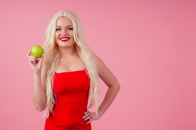 Foto retrato de uma jovem mulher loira sorridente feliz com maçã verde no fundo do estúdio rosa.