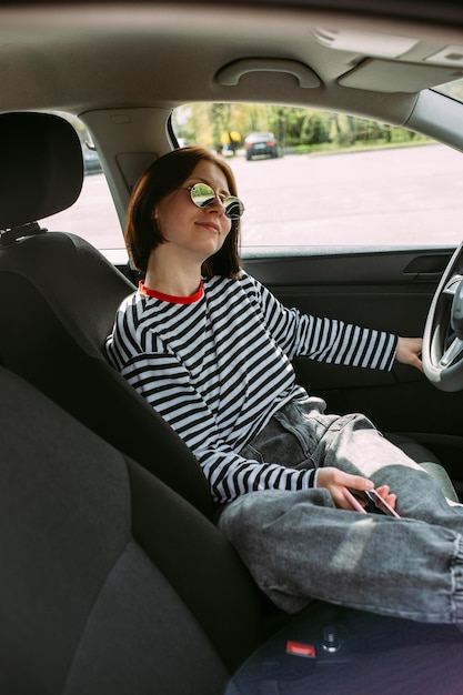 Foto retrato de uma jovem mulher morena dirigindo um carro usando um smartphone