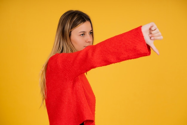 Retrato de uma jovem mulher mostrando o polegar para baixo a alguém em pé contra um fundo isolado.