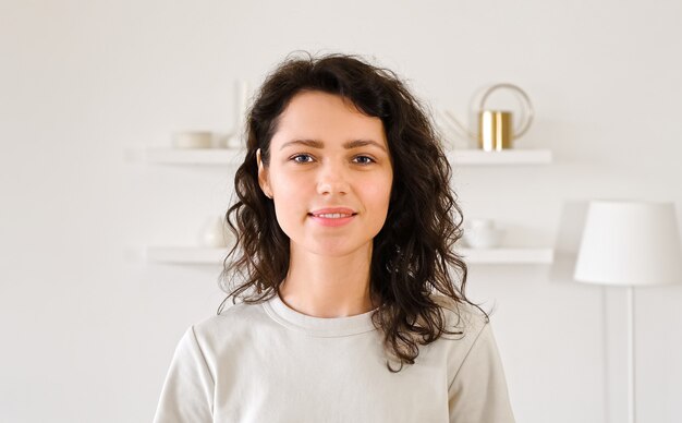 Foto retrato de uma jovem mulher olhando para a câmera e sorrindo. millinale garota com cabelo encaracolado em um interior claro.