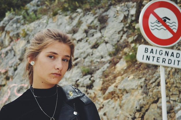 Retrato de uma jovem mulher por um sinal de informação contra uma rocha