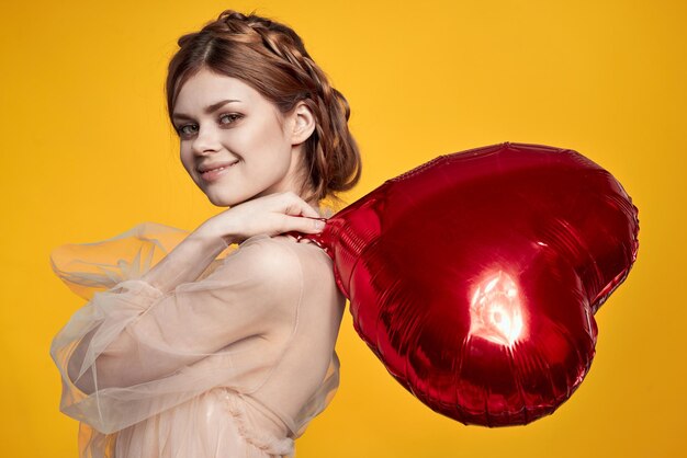 Foto retrato de uma jovem mulher segurando uma forma de coração contra um fundo amarelo