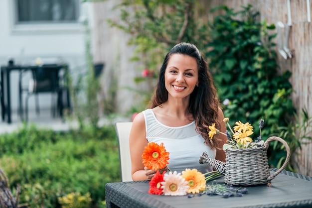 Retrato de uma jovem mulher sentada na mesa de madeira e aranging um buquê de flores.