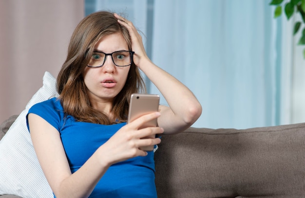 Retrato de uma jovem mulher surpresa e chocada olhando para a tela de seu celular