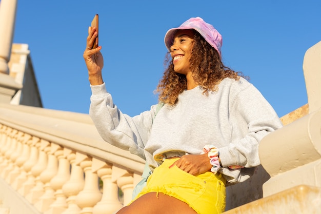 Retrato de uma jovem negra atraente sentado e falando com o telefone celular ao ar livre, sem máscara.