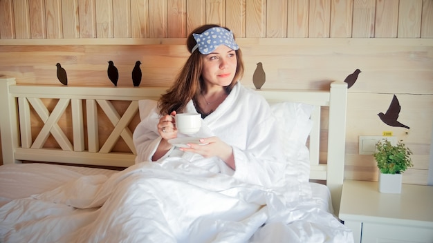 Retrato de uma jovem no banheiro deitada em um quarto de hotel e bebendo café