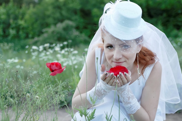 retrato de uma jovem. noiva em um vestido branco e chapéu cheira uma flor vermelha
