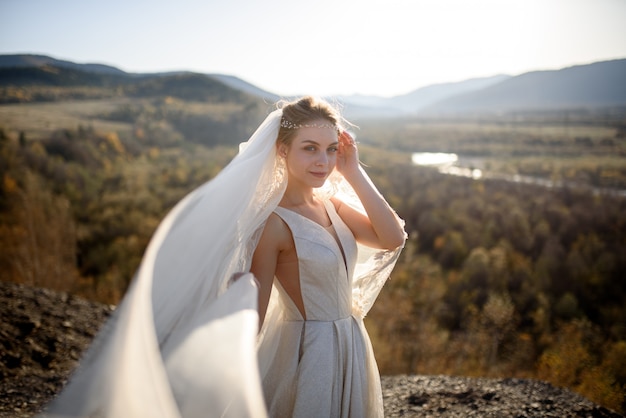 Retrato de uma jovem noiva linda nas montanhas com um véu. O vento desenvolve um véu. Fotografia de casamento nas montanhas.